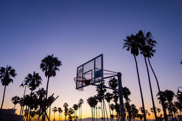 Silhouettes in the colorful sunset sky of palm trees, basketball hoops, and other things at Venice Beach in Los Angeles, California.  - Powered by Adobe