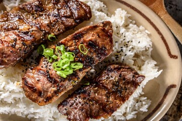 Mouthwatering Kalbi Delight: Top Close-Up of Delicious Grilled Kalbi on Steamed White Rice, Sizzling in a Cast Iron Pan, in 4K Resolution