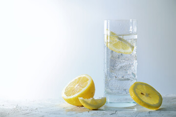 Carbonated soda water with ice cubes and lemon in a drinking glass, refreshing drink against a...
