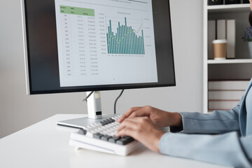 Close up view of young businesswoman typing on keyboard computer while analyzing graph and trend in her office room.