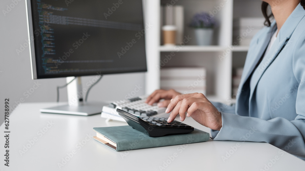 Poster Close up view of young programmer working on her coode while calculating result with calculator.