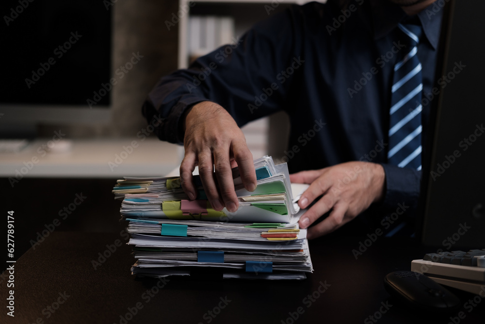 Poster Close up view of businessman woking and gathering information from stack of document, working overtime at night.