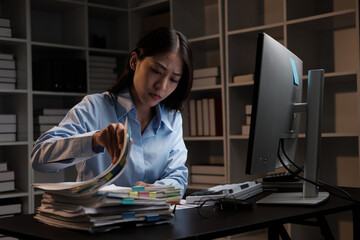 Young adorable Asian businesswoman working with work document during the night, working overtime at...