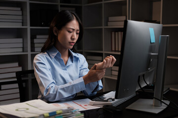 Young beautiful Asian businesswoman having a wrist pain, touching her wrist after working for a very long time.