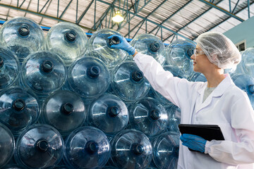 Caucasian women scientist with lab cote inspect quality of drinking water inside of the production line factory while using digital tablet to check cleanliness and standard, quality assurance