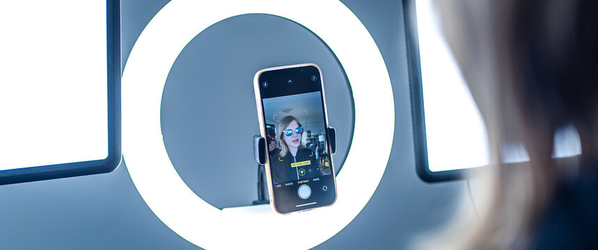 Young woman making photo or video content for social media with smartphone and light of ring lamp. Influencer makes broadcast communicates with followers in social networks.
