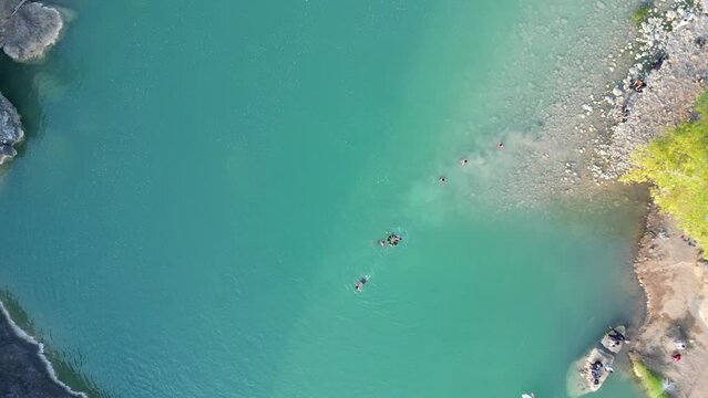 Aerial view of canoe boats in mountain river with turquoise water with rock cliffs. People kayaking, canoeing, and swimming in Kedung Jati Parang, Selopamioro, Imogiri, Bantul, Yogyakarta. 4k footage