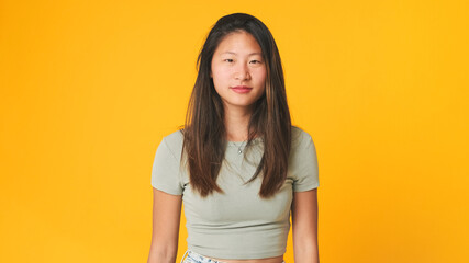 Girl in gray top looking at camera, isolated on yellow background in studio