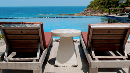 Empty beach chairs and a cocktail table by the pool. Sunny day at a tropical resort. Concept of peaceful vacation by the ocean.