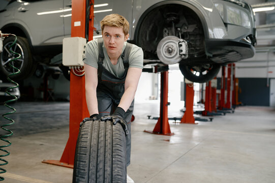 Male mechanic wearing gloves rolling tire for replacement at car service