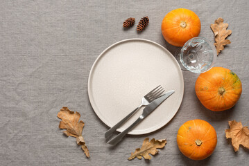 Autumn table setting. Beige plate, cutlery, decorative pumpkins on a grey linen tablecloth. Top view, flat lay, selective focus. Thanksgiving Day.