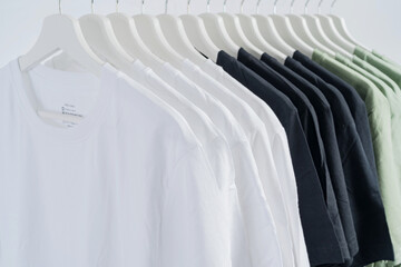 close up collection of black-white and green color t-shirt hanging on wooden clothes hanger