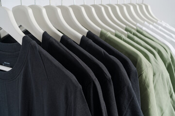 close up collection of black-white and green color t-shirt hanging on wooden clothes hanger