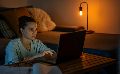 Young woman working at home at night on a project using a laptop.