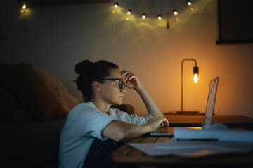 Young woman working at home at night on a project using a laptop. Problems with long hours...