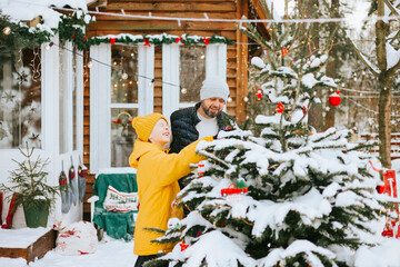 family dad and cute teenage boy decorate Christmas tree near front door porch of village...