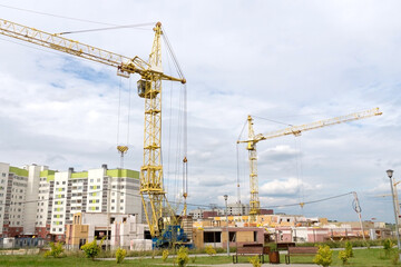 Fototapeta na wymiar Tower cranes and unfinished buildings on background of blue sky with white clouds. Housing construction, apartment blocks in city