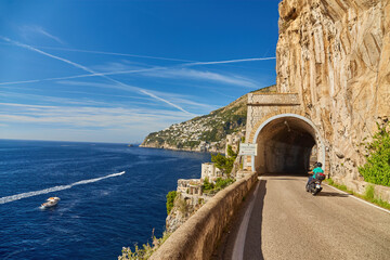 Scooter drives along the road along the Amalfi coast, approaching the tunnel Conca dei Marini - obrazy, fototapety, plakaty
