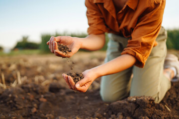 Experienced farmer woman touches the soil with her hands, collects it, checks health and quality of soil before growing seeds, vegetables, plants. Business, agriculture concept.