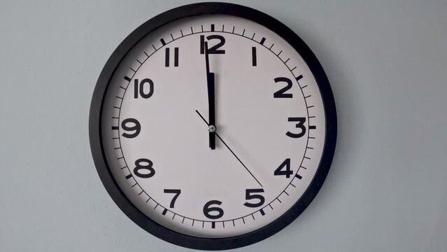 Closeup of White Clock Face on white wall clock, arrows show 11:55 to 12:00