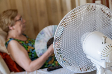 Electric fan cooling an elderly woman sitting on the sofa in the living room.