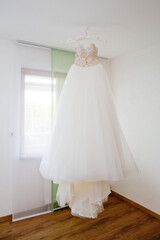 Fototapeta na wymiar The delicate bride's dress is hanging in room. Selective focus.