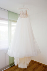 Fototapeta na wymiar The delicate bride's dress is hanging in room. Selective focus.