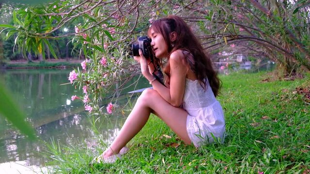 Young asian woman in white dress sitting and taking camera with flowers in the park