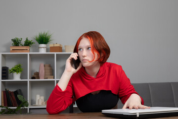 Frustrated annoyed focused teen girl holding smartphone, attentively listening to bad news, talking serious conversation, sitting at home in his room at the table with a laptop