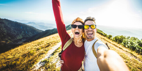 Cheerful couple of hikers taking selfie on top of the mountain - Millennial guy and girl enjoying...