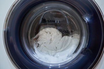 Wet white laundry in the drum of the washing machine. Close-up glass door from the washing machine with space for copying. High quality photo