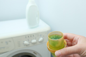 Female hand using or filling detergent in the washing machine. Pour green washing liquid, wash...