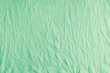 Wrinkled, crumpled green fabric texture background. Wrinkled and creased abstract backdrop of cotton jersey textile, wallpaper with copy space, top view.