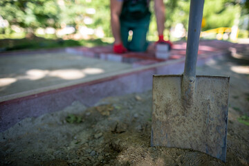 In the foreground, a shovel stuck in the ground and construction workers in the background.