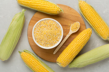 Corn groats with fresh cobs on concrete background, top view