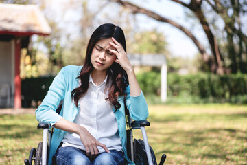 Fototapeta premium Woman on wheelchair concept, Young asian woman on wheelchair in the garden and touching hands to rubbing nose while feeling stressed and exhausted