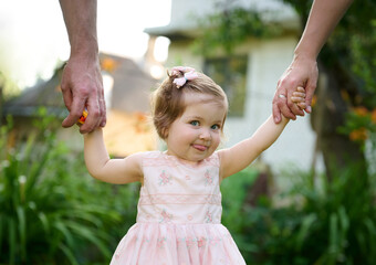 Lovely family walking holding hands, adopted child being supported by loving parents. Girl holds...
