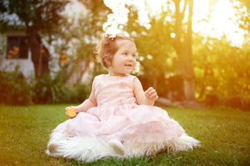 Adorable girl on the grass in the garden. Close up portrait. Happy little girl in summer scenery. Sweet small kid outdoors.