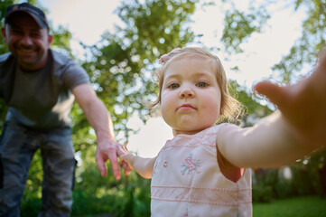 Lovely father walking holding hands, adopted child being supported by loving parents. Girl holds hands of her parents and jumps. Cropportrait of the cute adorable small girl in dress.