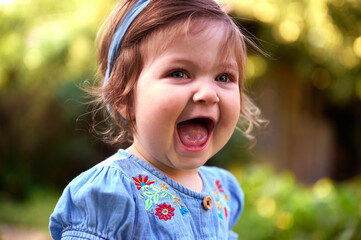 Adorable girl on the grass in the garden. Close up portrait. Happy little girl in summer scenery. Sweet small kid outdoors.