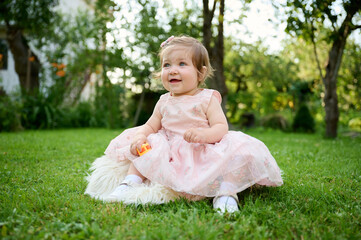 Adorable girl on the grass in the garden. Close up portrait. Happy little girl in summer scenery. Sweet small kid outdoors.