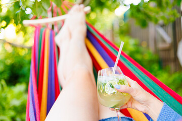 Young woman with a glass of cocktail resting lying in hammock in garden
