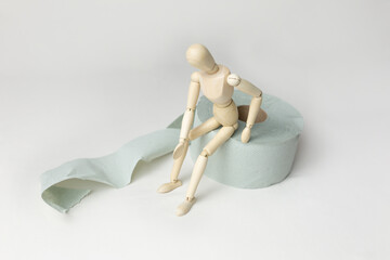 a wooden mannequin sits on a roll of toilet paper. The concept of digestive problems. constipation, poisoning
