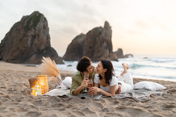 Happy couple having romantic date picnic on the beach, lying on blanket and drinking wine, having...