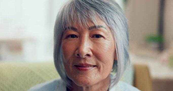 Face, retirement and happy with a senior asian woman in the living room of her home closeup. Portrait, wrinkles and gray hair with an elderly female pensioner sitting in her house to relax alone