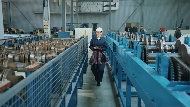 Close up woman engineer in safety uniform and hard hat walking use tablet computer checks production processes in factory. Inspector in warehouse.