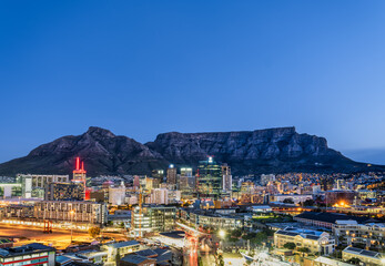 Wide angle shot of Cape town City buildings and streets lit up at night with the table mountain in...