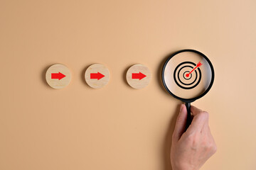 Target goal and arrow icons with magnifying glass on wooden blocks for business strategy planning...