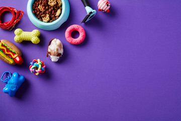 Pet toys and supplies with bowl of dry food on purple background. Flat lay, top view.