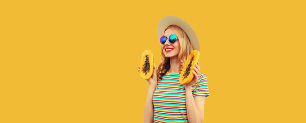 Summer portrait of happy cheerful young woman having fun with fresh papaya fruits wearing straw hat, sunglasses on yellow background